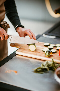 person slicing zucchini on wooden board in modern kitchen setting.