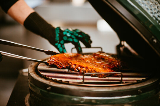 grillmaster flips succulent ribs on large green outdoor grill.