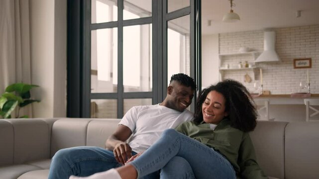 African American happy family love couple girl guy man woman male female fall on couch rest home weekend relocation moving day own house tired smile homeowners tenants relaxing cuddling cozy on sofa
