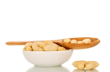Roasted peanuts in a white ceramic saucer and with a wooden spoon, close-up, isolated on a white background.