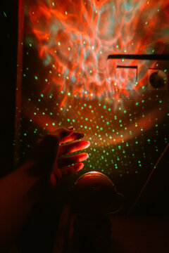 Colorful light projections on wall with hand reaching out at night.