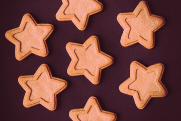 A top view of delicious gingerbread cookies in the shape of stars, lying on a purple background that depicts the night sky with stars. It's a holiday scene.