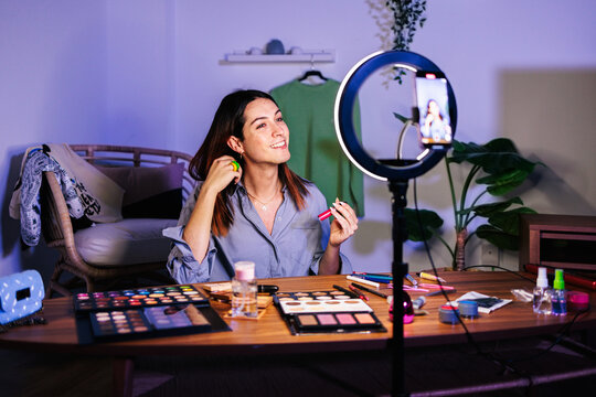 A person with makeup products while recording with a smartphone
