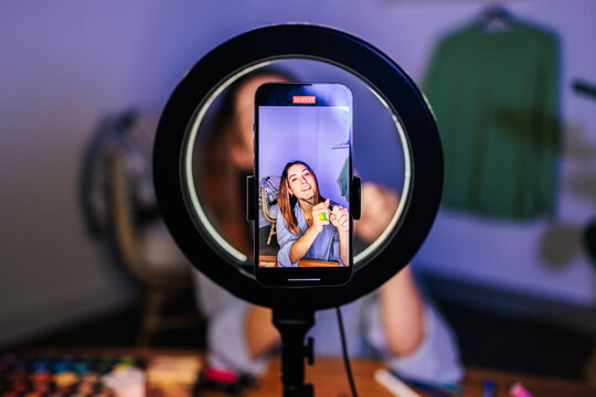 A person smiling while applying makeup is recorded on a smartphone