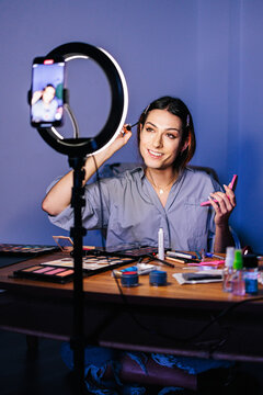 A person applies makeup and smiles while being filmed on a smartphone