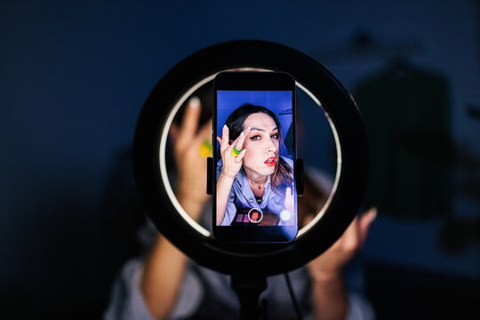 A smartphone mounted in a ring light displays a person applying makeup