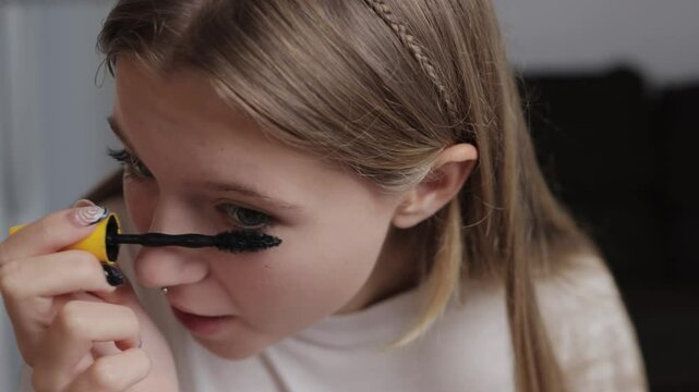 Young woman applying mascara while looking into a mirror, finishing a simple morning makeup routine at home. Focus on enhancing natural beauty through careful makeup techniques