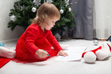 A little girl draws on an album sheet with colored pencils.