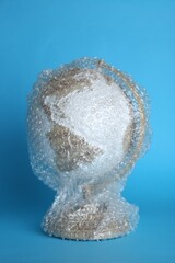 Globe packed in bubble wrap on turquoise background. Environmental conservation