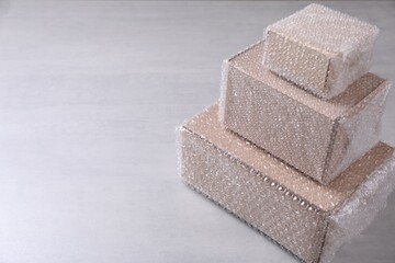 Cardboard boxes covered with bubble wrap on light grey table. Space for text