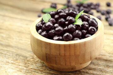 Ripe acai berries and leaves in bowl on table, closeup