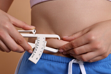 Woman measuring body fat with caliper on beige background, closeup