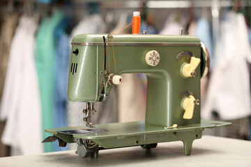 Vintage sewing machine with thread on white table in workshop, closeup