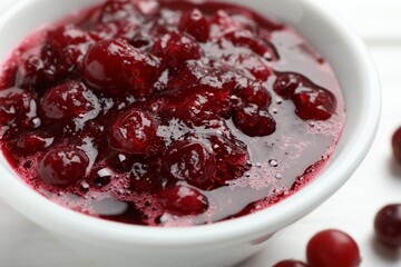 Tasty cranberry sauce in bowl and berries on table, closeup