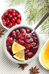 Tasty cranberry sauce in bowl, berries, orange, anise and fir branches on white wooden table, flat lay