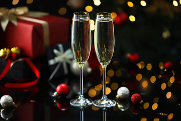 Delicious champagne in glasses and Christmas decor on black mirror surface against blurred lights, closeup