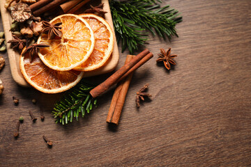 Different spices, dried orange slices and fir tree branches on wooden table, flat lay with space for text. Christmas season