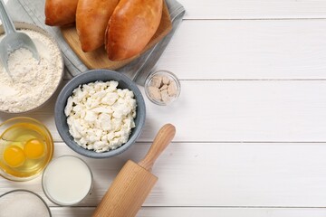Delicious pirozhki (stuffed pastry pies) and ingredients on white wooden table, flat lay