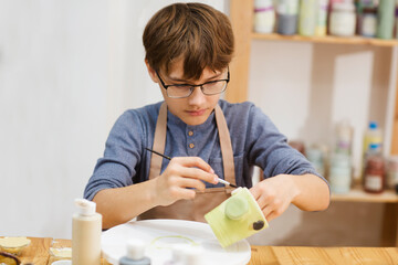 teenager boy paint the clay mugs they made in pottery school.  Children arts a crafts class in...