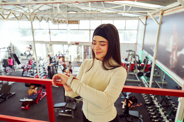 Fototapeta premium Latina woman looking at an app on her smartwatch at the gym, morning routine and wellness concept