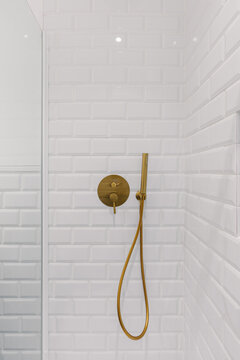 A modern shower with a sleek gold handheld showerhead and control knob