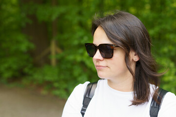 Beautiful smiling dark-haired girl in a white T-shirt and with a backpack on her shoulders in the summer on a trip. Pedestrian wanderung concept