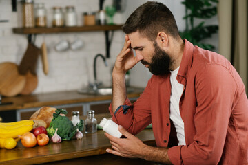 A young bearded man with a headache examining medication at home. Medicines effective treatment. Pharmacy concept.