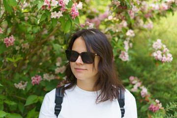 Beautiful smiling dark-haired girl in a white T-shirt and with a backpack on her shoulders in the...
