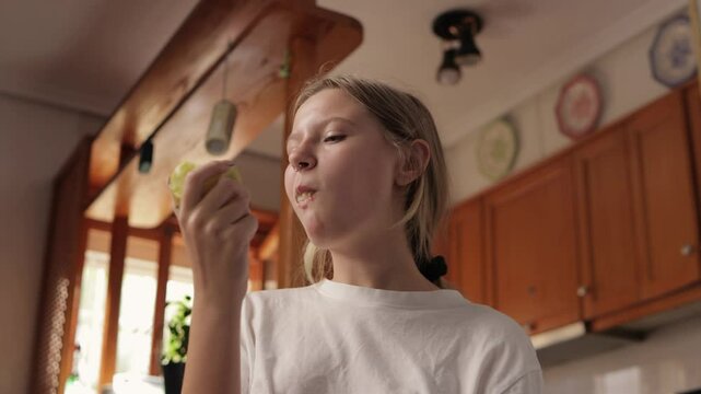 Young woman enjoys a crisp green apple in her kitchen, savoring each bite and appreciating the fresh flavor and health benefits of this nutritious snack
