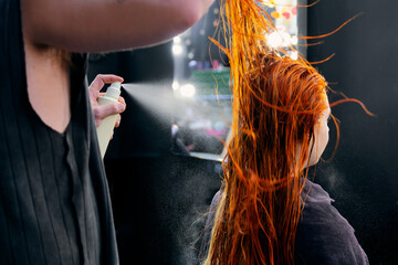 Hair stylist applying product to vibrant red hair in a salon