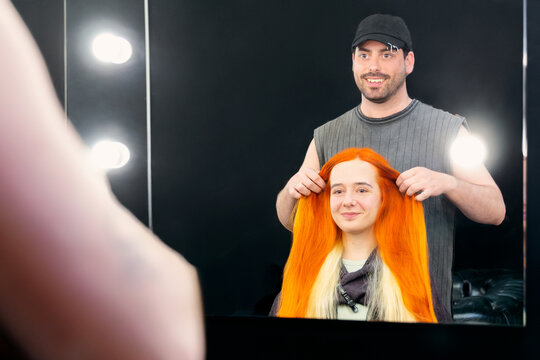 Hair stylist adjusting vibrant wig on smiling client at salon