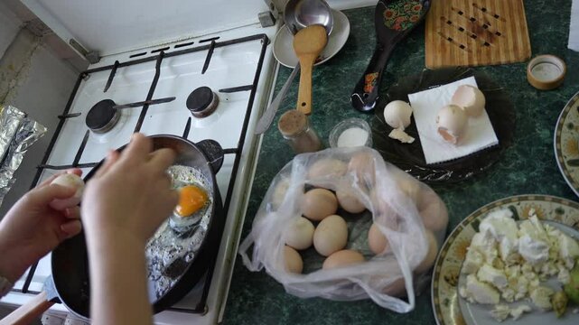 A person is cracking an egg into a pan while preparing a hearty breakfast. The kitchen is warm and inviting, filled with fresh ingredients and cooking utensils scattered around.