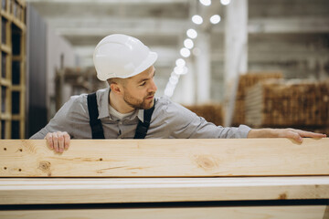 Construction worker checking quality of wooden planks in warehouse