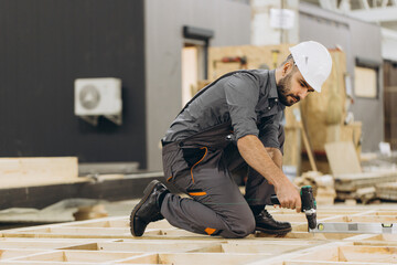 Carpenter building wooden frame house using electric screwdriver in workshop