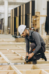 Construction worker building wooden frame using spirit level and drill in modular building industry