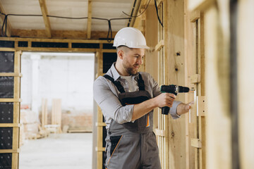 Construction worker building wooden frame house using cordless drill