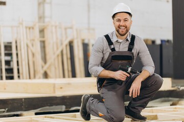 Carpenter kneeling and holding cordless drill in modular building workshop
