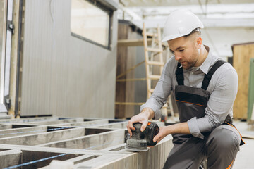Carpenter sanding wooden plank in modular building construction site