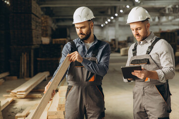 Builders inspecting wooden plank in modular building industry factory