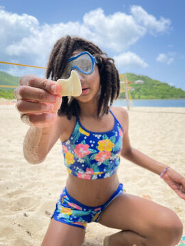 Preteen with swim goggles sitting on a sandy beach holding a seashell