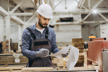 Carpenter reading blueprint in lumber processing factory for modular building