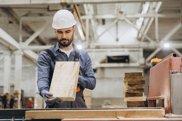 Carpenter inspecting wooden plank in modular building factory