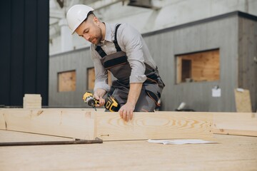 Carpenter using cordless drill assembling wooden frame for modular building
