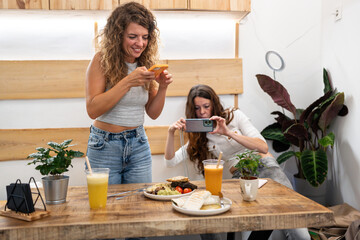 Two female friends taking photos of food in restaurant