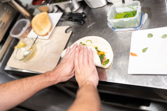 Chef folding a wrap with fresh vegetables in a restaurant kitchen