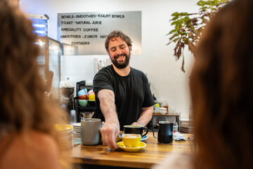Smiling barista serving coffee to customer in cafe