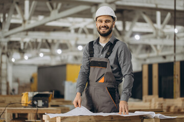 Smiling engineer reading blueprints in modular building factory