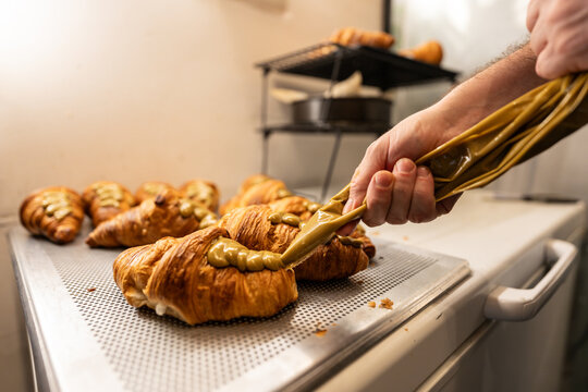 Baker filling croissants with pistachio cream using pastry bag