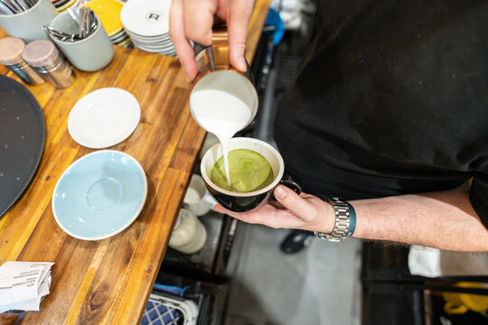 Barista pouring steamed milk into matcha green tea latte in cafe