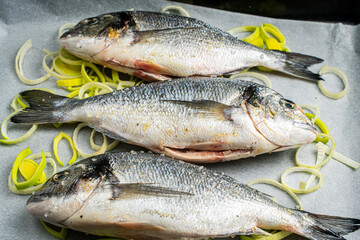 Raw dorado fish on baking paper with leeks cut into rings, ready to bake and cook.